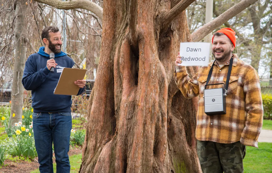 City staff stands in front of a large dawn redwood tree, with a member of the public holding a sign with the trees name.