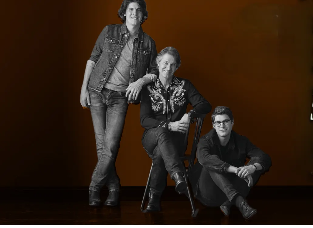 Three men pose together. One sits in a chair, another on the floor.